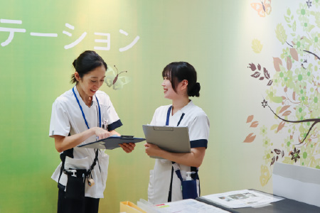 白いユニフォームを着用した2人の女性スタッフがカルテや書類を確認しながら笑顔で打ち合わせをしている様子