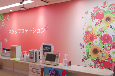 ひまわりなどの華やかなイラストが描かれたピンク色の壁面が特徴的な、明るいスタッフステーション(ナースステーション)の受付カウンターの様子