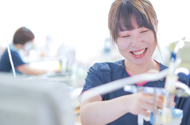 紺色のスクラブを着用した女性スタッフが、親しみやすい笑顔を浮かべながら手元の医療機器を扱っている様子